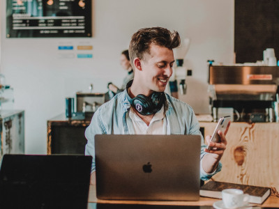Young male smiling at his phone while working in a coffee shop