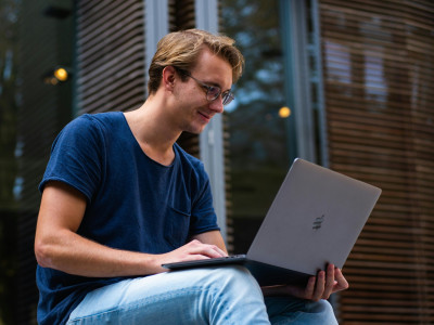 Young man smiling at his laptop, outdoor setting