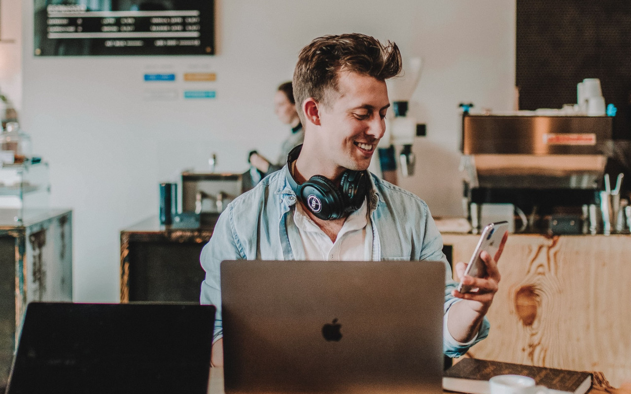 Young male smiling at his phone while working in a coffee shop