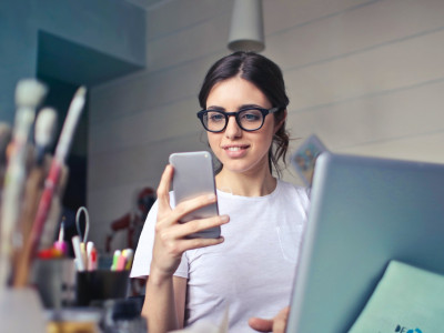 Young woman smiling at her phone while sitting at a desk surrounded by artistic tools